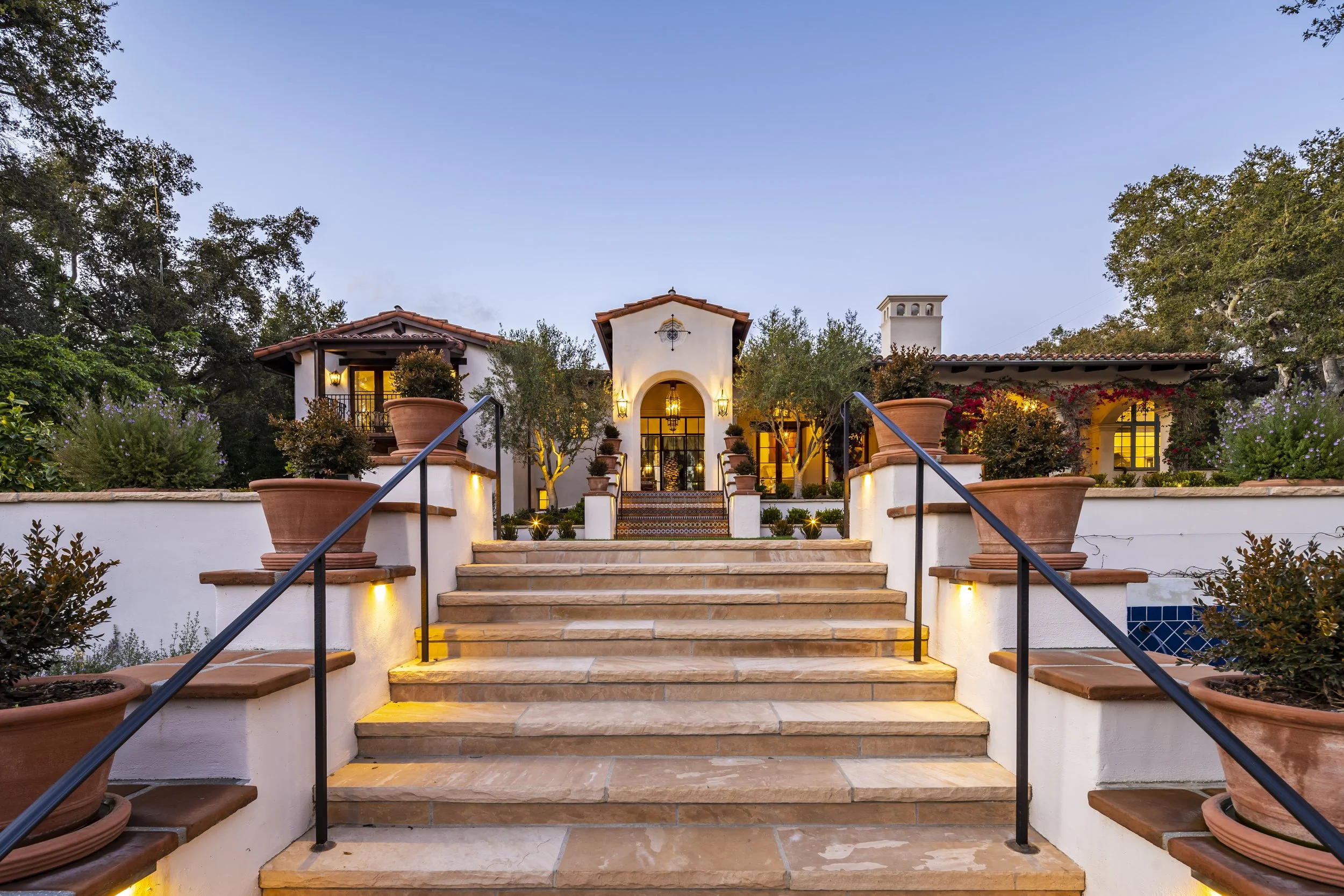 Front entrance of the East Valley Road Residence, showcasing a terracotta staircase with large planters, wrought iron railings, and a well-lit Spanish Colonial Revival facade.