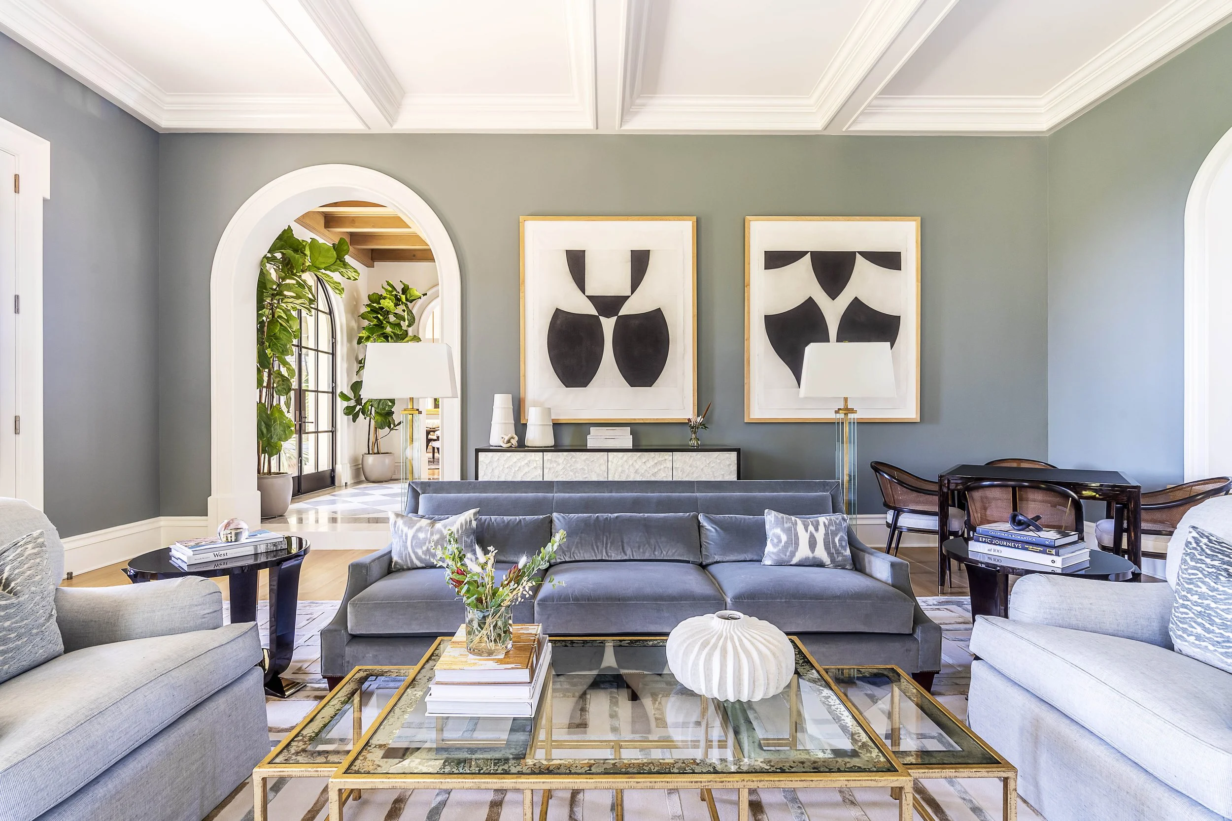 Modern living room with gray sofa, abstract artwork, and arched doorway, featuring glass coffee table and decorative accents, designed by The Warner Group Architects, Inc.
