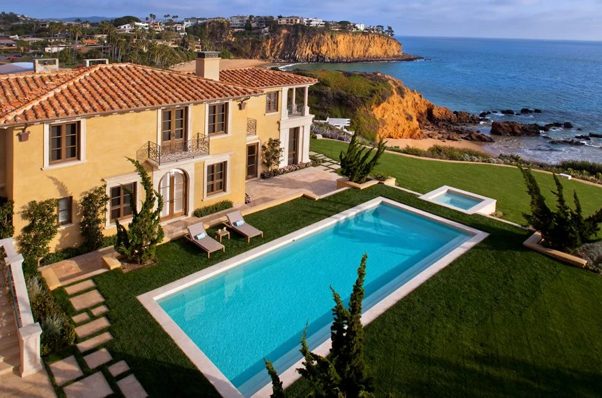 Luxury coastal villa with pool, green lawn, and ocean view.