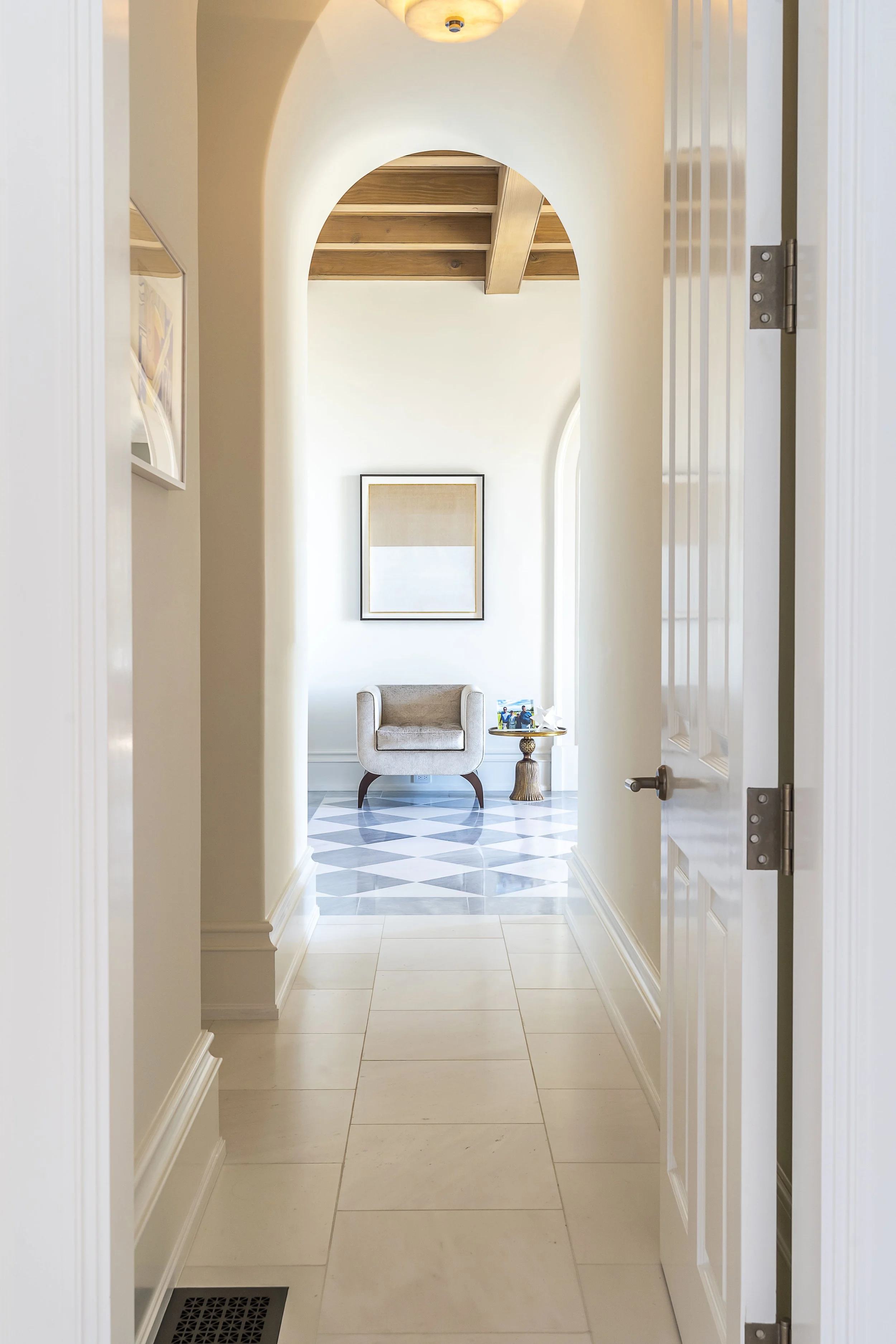 Elegant hallway with arched doorway and decorative chair, featuring a modern art piece, designed by The Warner Group Architects, Inc.