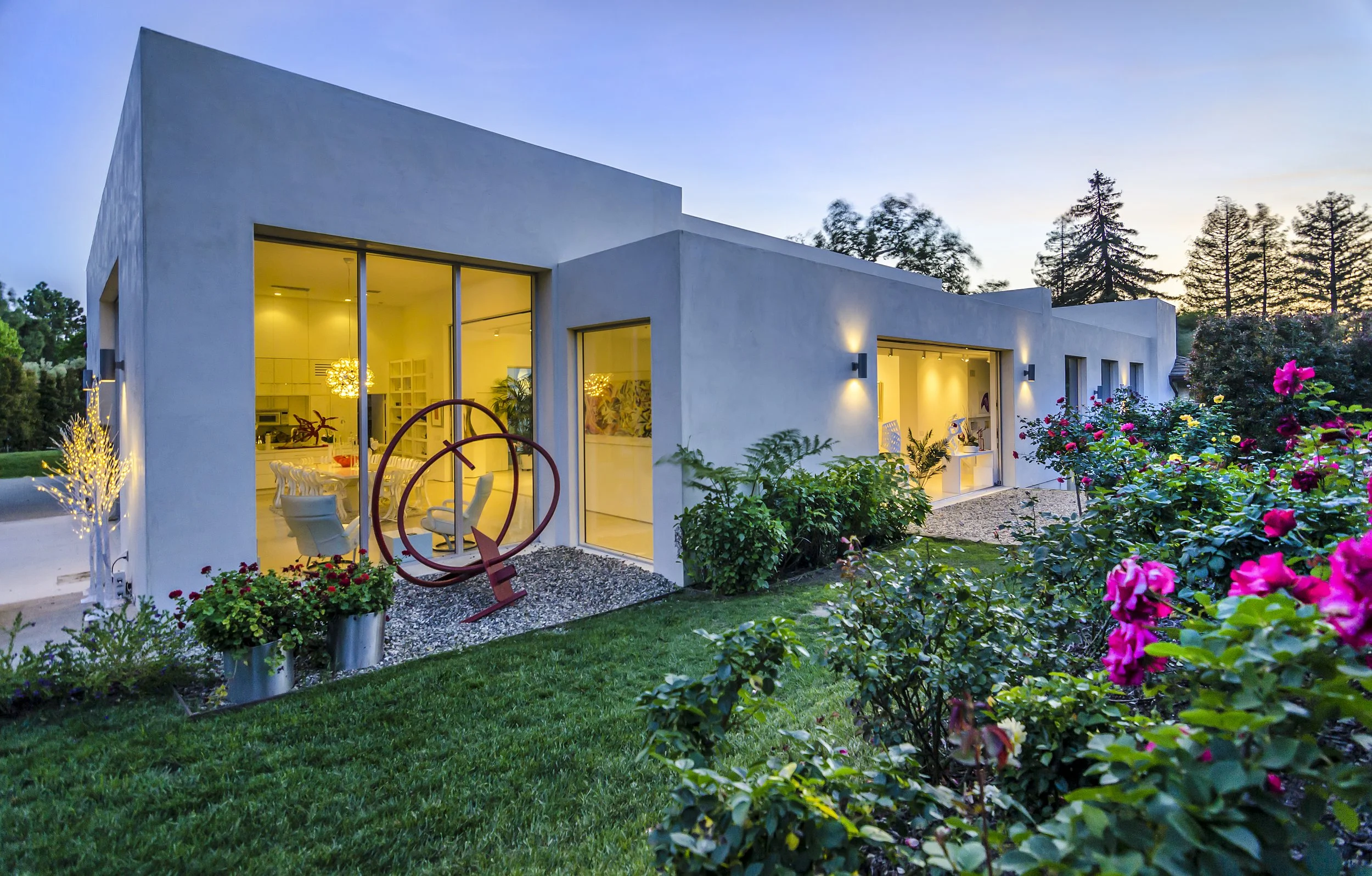 Evening view of a contemporary art-filled garden with rose bushes and outdoor sculptures
