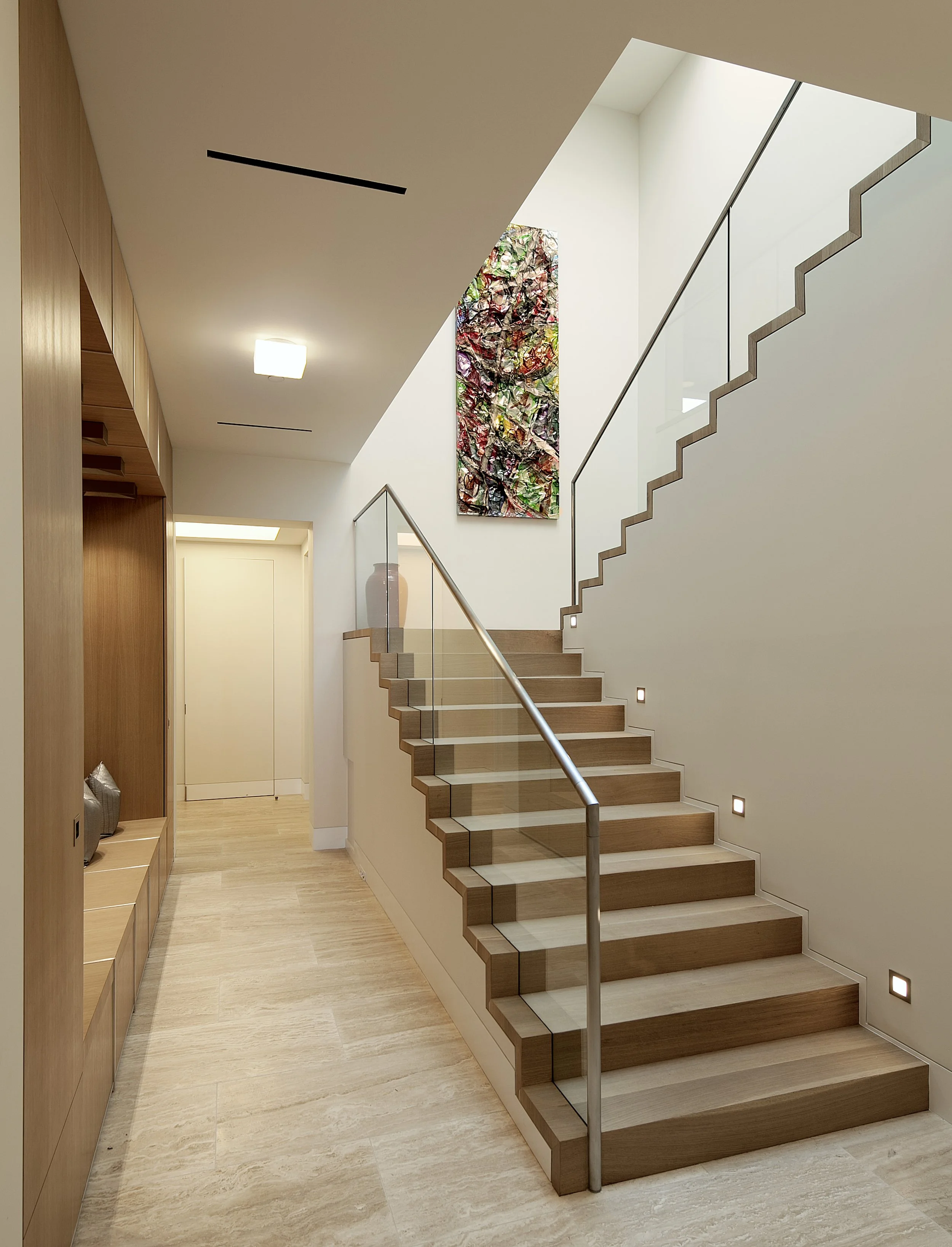 Modern staircase with glass railing and wall art in a contemporary interior.