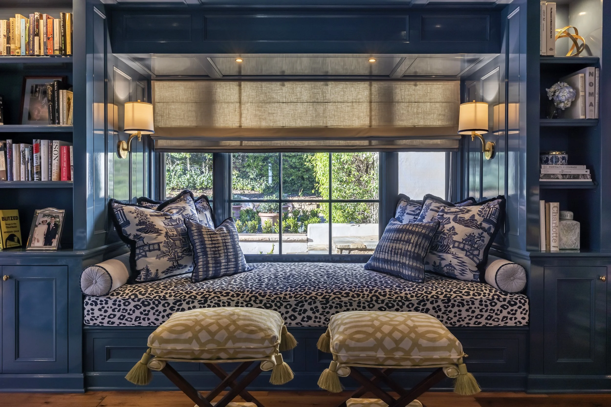 Cozy window nook with leopard print cushions, blue pillows, and built-in bookshelves with various books and decor items.