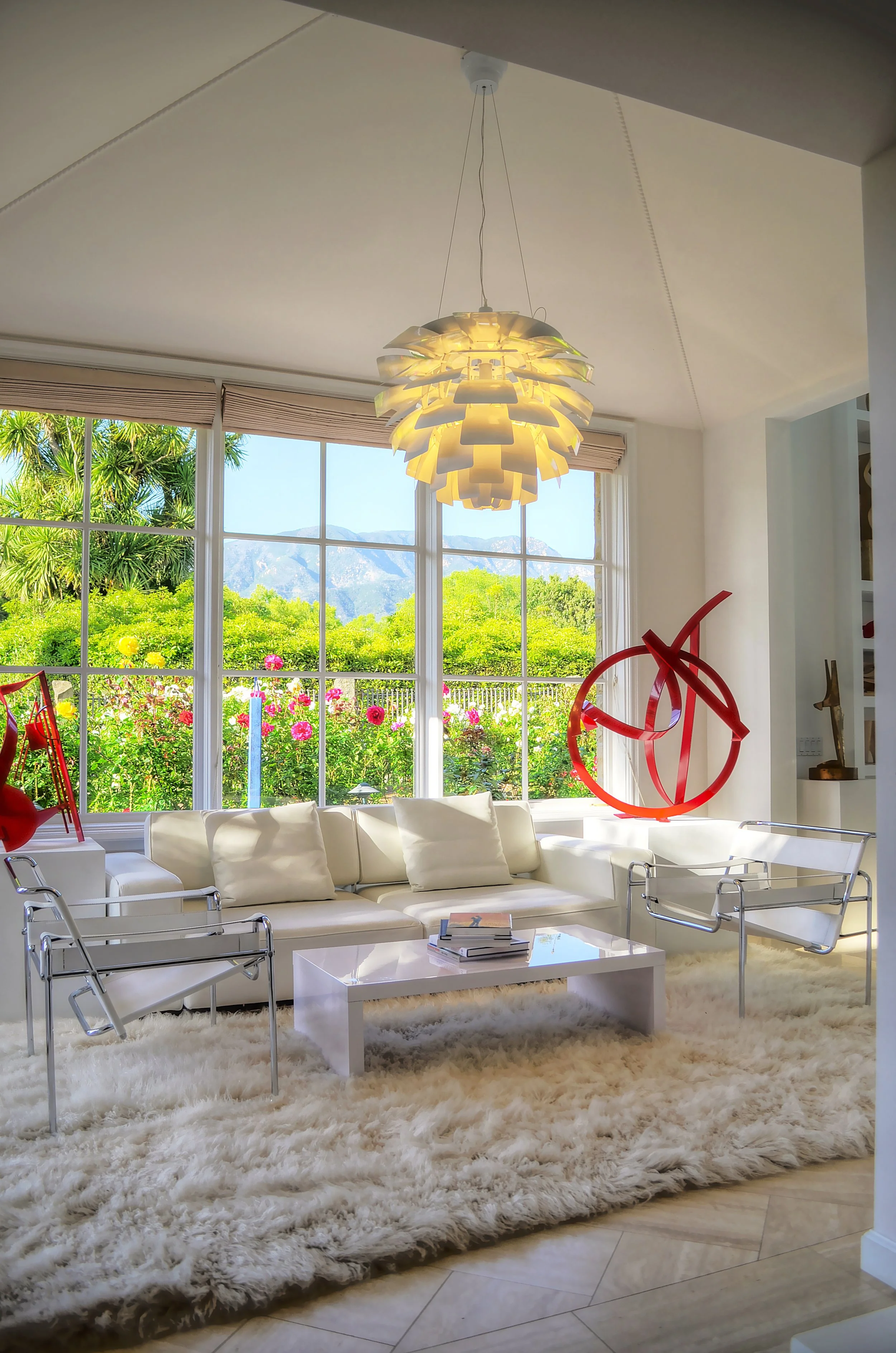 Modern luxury living room featuring a contemporary sculpture against a scenic backdrop of vibrant greenery and distant mountains. The clean, minimalist aesthetic complements the spacious layout, creating a serene and modern atmosphere.