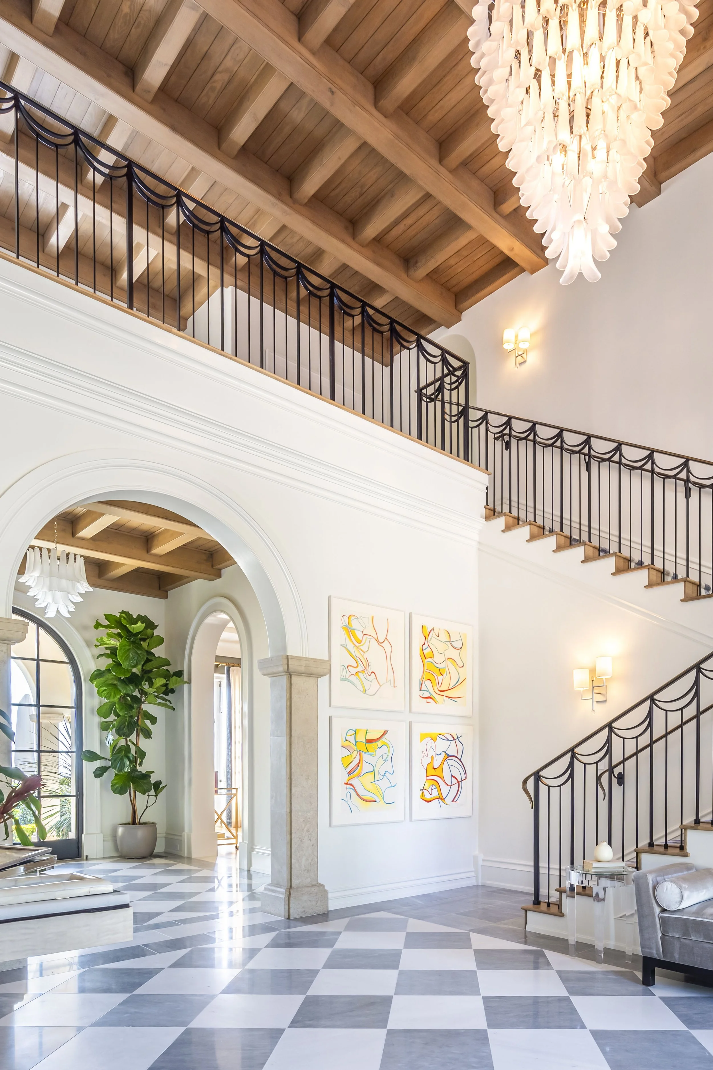 Grand foyer with vaulted ceilings, elegant staircase, and modern artwork, featuring checkered marble flooring and a large chandelier, designed by The Warner Group Architects, Inc.