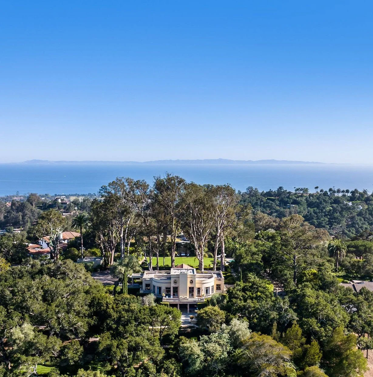 Aerial view of a large house surrounded by trees with an ocean in the background.